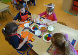 Dzieci wybierają kolory galaretek do krojenia z talerzyków na środku stołu.